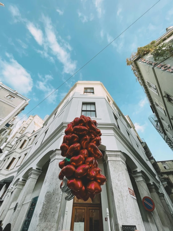 a bunch of red balloons hanging from the side of a building, by Emma Andijewska, unsplash contest winner, street art, realistic 8k bernini sculpture, turkey, worm\'s eye view, giant flowers