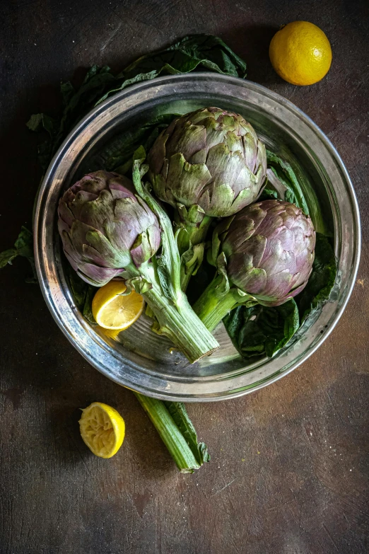 a bowl of artichokes and lemons on a table, a portrait, pexels, greens), against dark background, made of glazed, stuffed