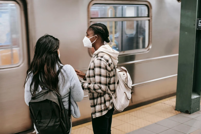 a couple of women standing next to a train, pexels contest winner, medical mask, mta subway entrance, people watching, thumbnail