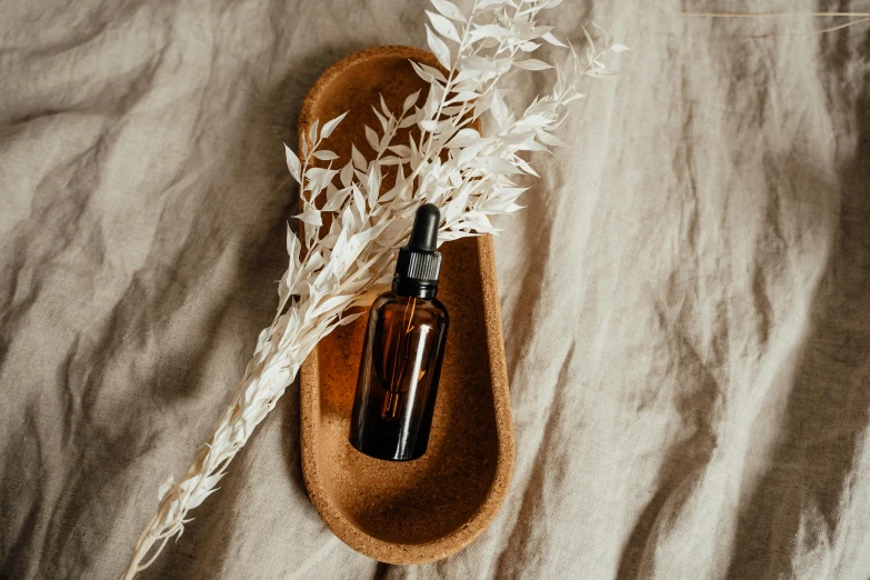 a bottle of essential oil sitting on top of a wooden spoon, by Emma Andijewska, linen canvas, thumbnail, skincare, brown