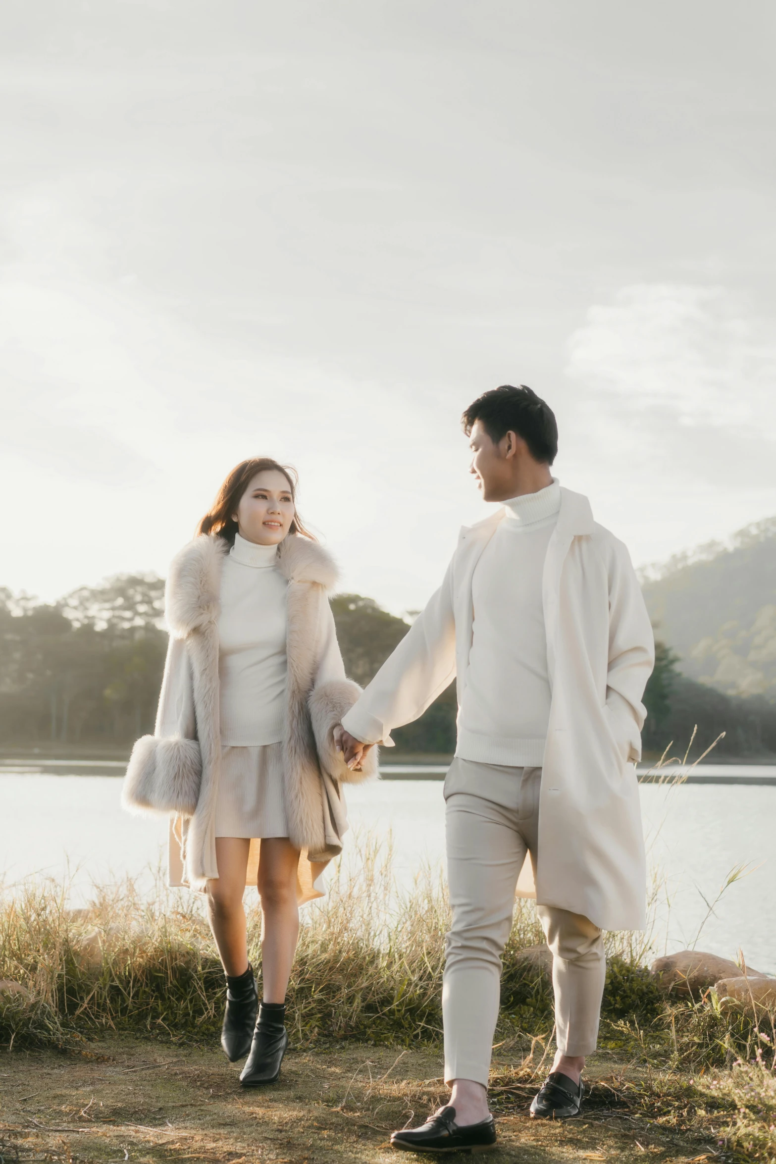 a man and woman holding hands in front of a lake, by Basuki Abdullah, trending on pexels, romanticism, light cream and white colors, winter, 15081959 21121991 01012000 4k, handsome man