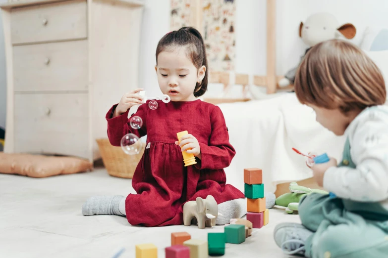 two children sitting on the floor playing with soap bubbles, pexels contest winner, building blocks, wearing a red outfit, tiny girl looking on, thumbnail