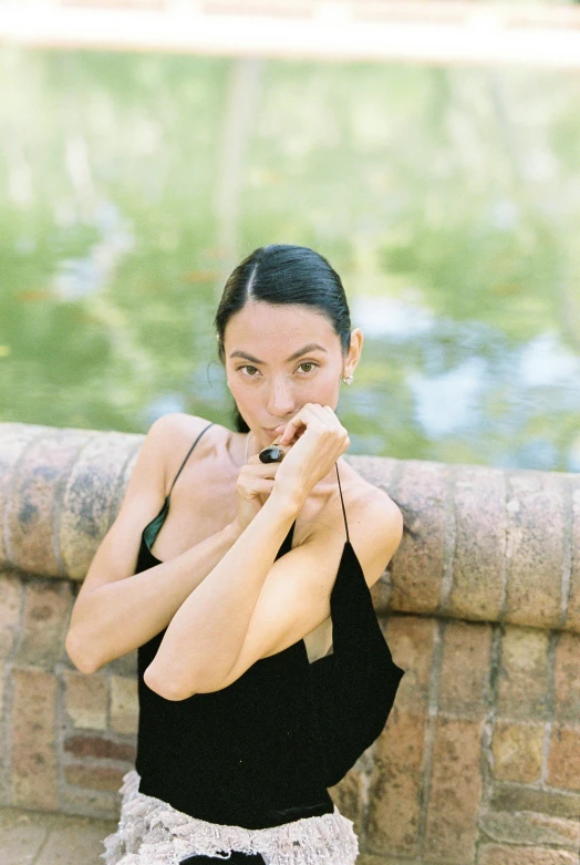 a woman in a black dress holding a cell phone, inspired by Li Di, unsplash, arabesque, squatting down next to a pool, posing with crossed arms, kiko mizuhara, yoga meditation pose