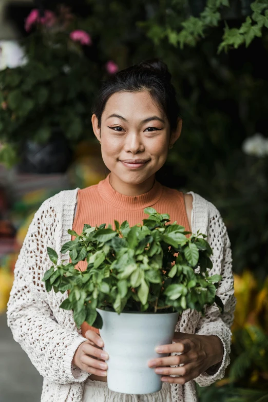 a woman holding a potted plant in her hands, a portrait, inspired by Ruth Jên, pexels contest winner, star trek asian woman, flower shop scene, promotional image, looking towards camera