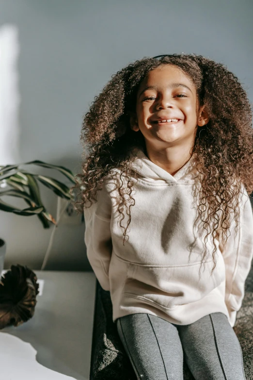 a little girl sitting on top of a bed next to a teddy bear, long afro hair, wearing a hoodie and sweatpants, covered in plants, portrait featured on unsplash