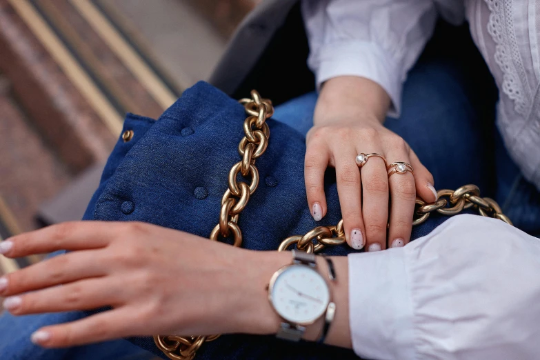 a woman sitting on a bench holding a purse, by Julia Pishtar, trending on pexels, aestheticism, holding gold watch, double denim, ((chains)), wearing lab coat and a blouse