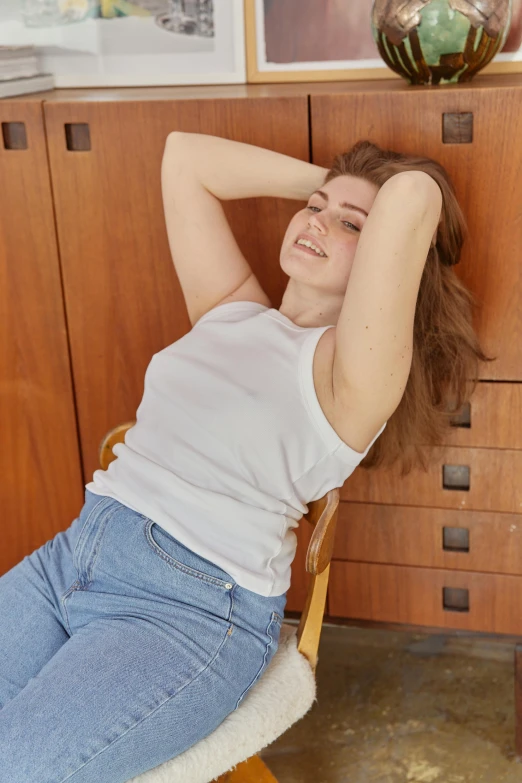 a woman laying on a chair in a room, inspired by Elsa Bleda, trending on unsplash, renaissance, outfit : jeans and white vest, wearing : tanktop, slightly overweight, 70s photo