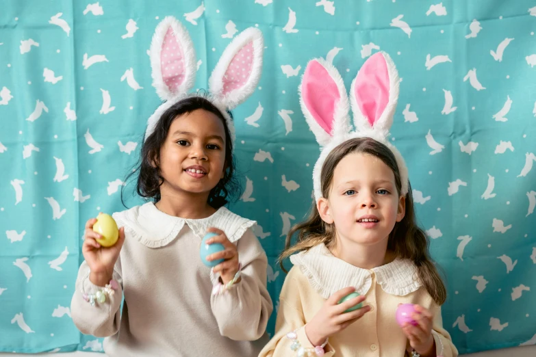 a couple of little girls standing next to each other, pexels contest winner, pointy bunny ears, eggs, cyan photographic backdrop, repeating pattern