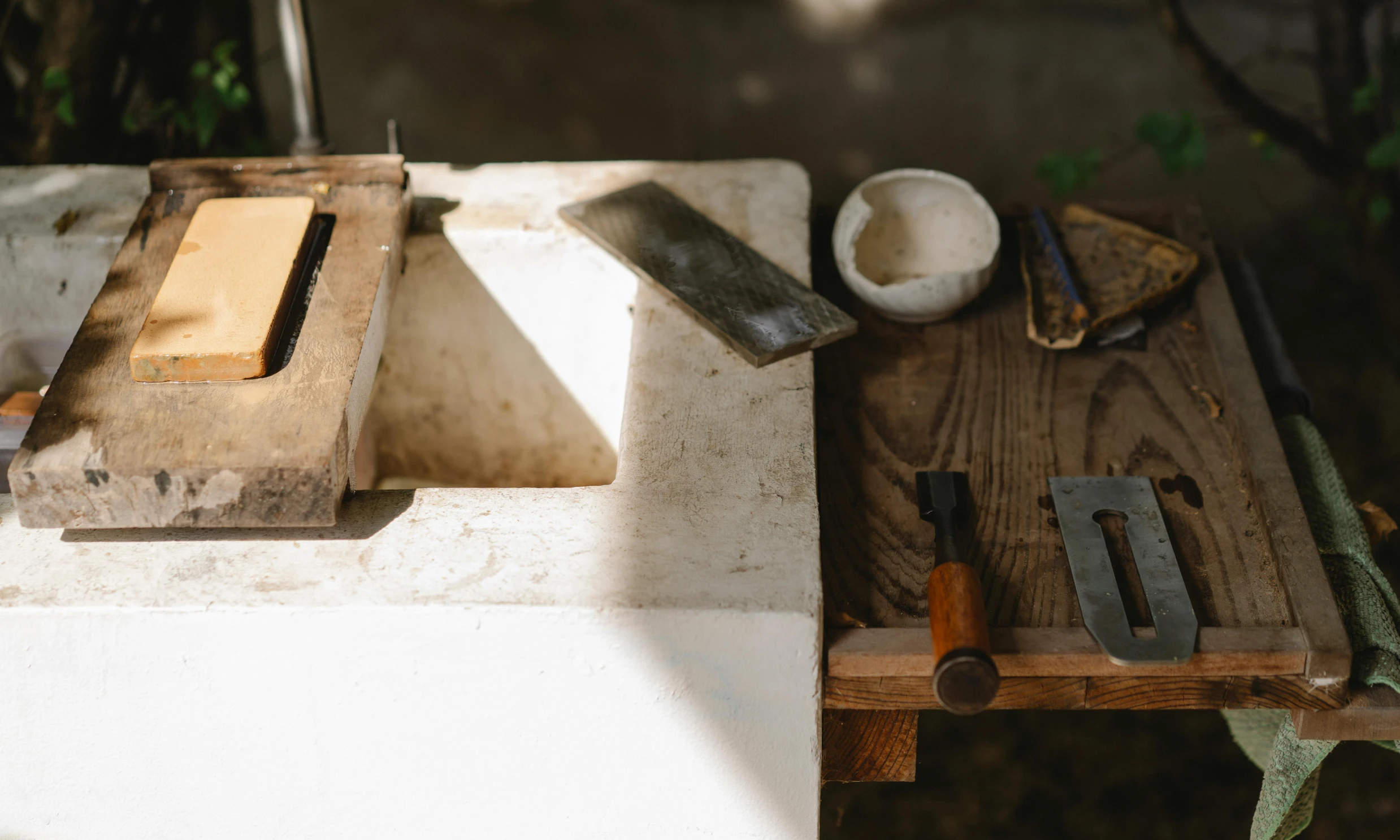 a wooden cutting board sitting on top of a table, a marble sculpture, inspired by Constantin Hansen, trending on unsplash, arts and crafts movement, scrap metal on workbenches, natural light outside, working in the forge, fixing a leaking sink