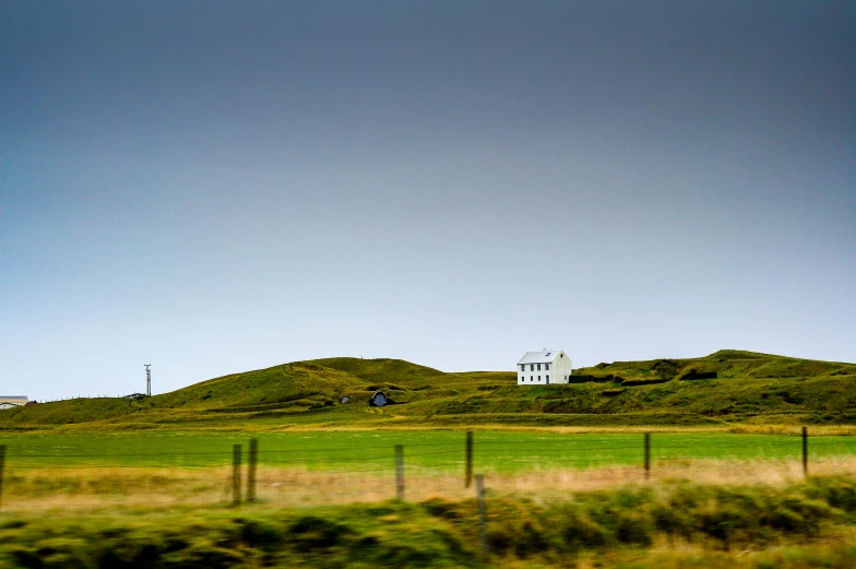 a white house sitting on top of a lush green hillside, unsplash, fantastic realism, icelandic landscape, archival pigment print, landscape from a car window, pembrokeshire