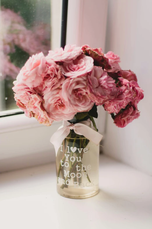 a vase filled with pink flowers sitting on a window sill, by Dulah Marie Evans, romanticism, saying, glass jar, etched inscriptions, super cute and friendly