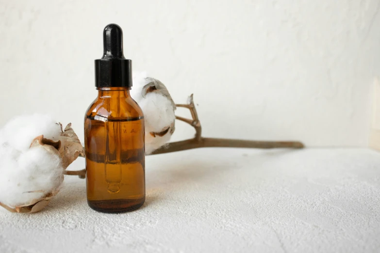 a bottle of cotton oil next to a branch of cotton, inspired by Lubin Baugin, trending on pexels, brown resin, background image, handcrafted, skincare