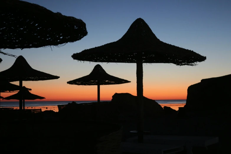 a group of umbrellas sitting on top of a sandy beach, during a sunset