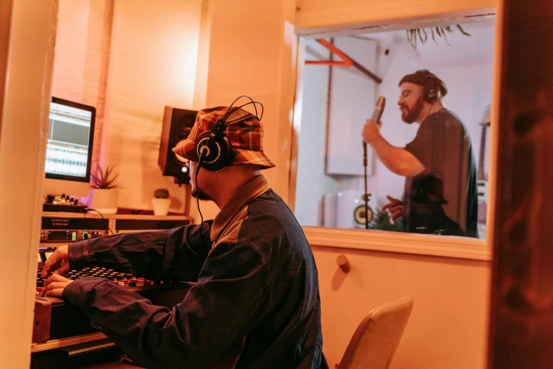 a man sitting at a desk in front of a computer, an album cover, by Lee Loughridge, unsplash, two buddies sitting in a room, sitting in front of a microphone, madhouse studio, lachlan bailey