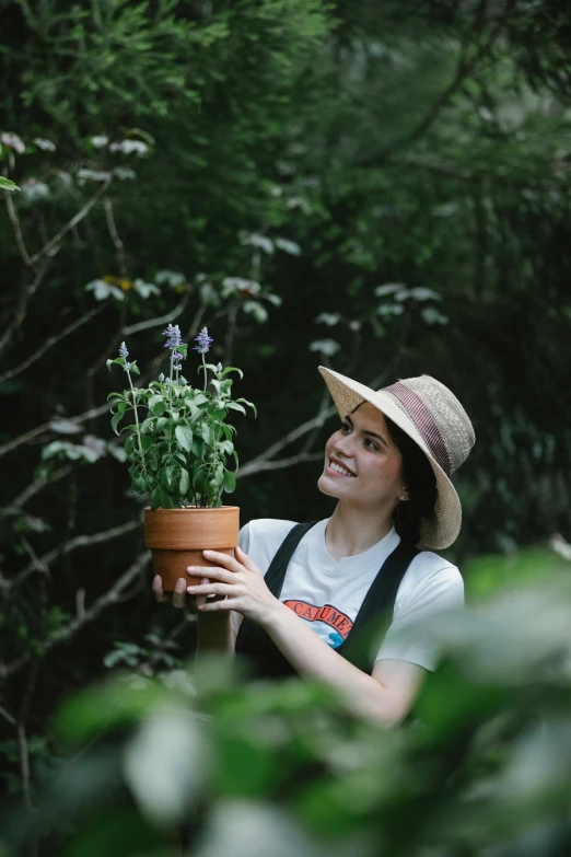 a woman in a hat holding a potted plant, lush surroundings, profile image