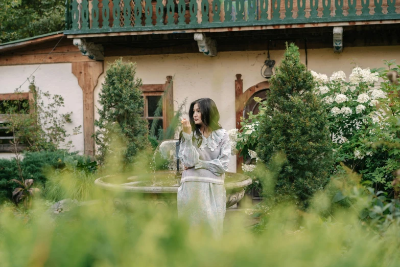 a woman standing in a garden next to a fountain, inspired by Elsa Bleda, pexels contest winner, art nouveau, standing outside a house, charli xcx, andrey tarkovsky, performing