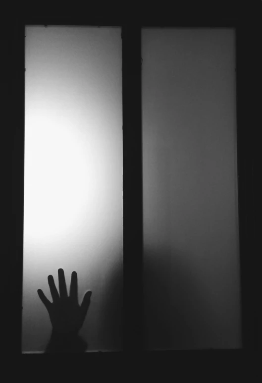 a person that is standing in front of a window, a black and white photo, by Lucia Peka, unsplash, conceptual art, glowing hands, leaning on door, crime, claustrophobic room