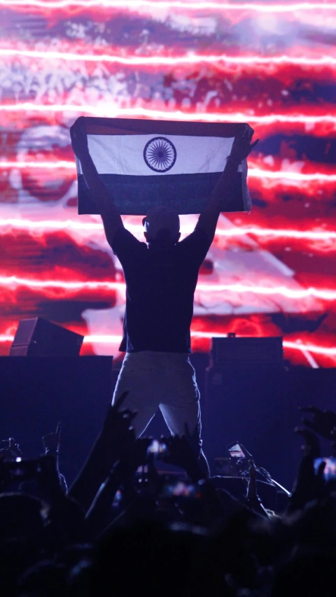 a man holding a flag in front of an american flag, an album cover, trending on reddit, symbolism, provocative indian, dj rave party, big head on stage, - n 9