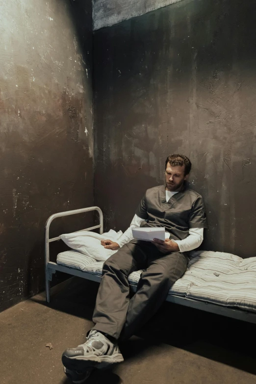 a man sitting on a bed in a jail cell, reading, artem, cast, bunker