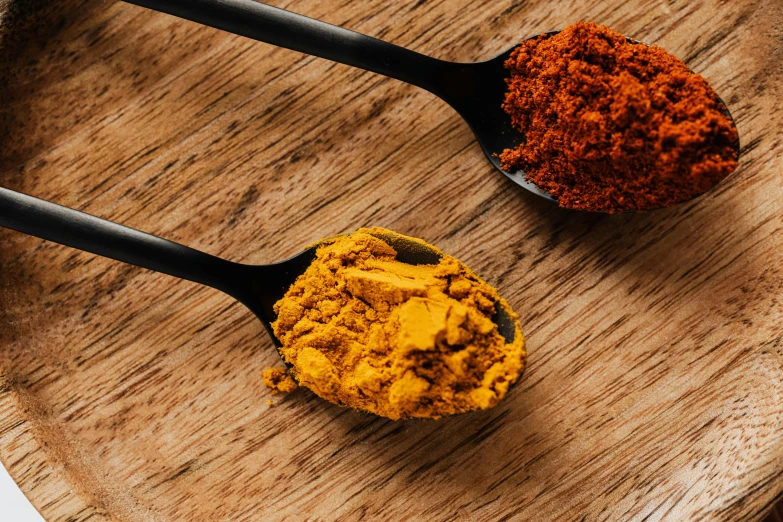 two spoons filled with spices on top of a wooden plate, by Julia Pishtar, trending on unsplash, yellow and orange color scheme, powder, malaysian, “ iron bark