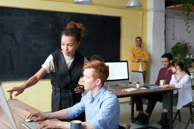 a couple of people that are sitting in front of a laptop, standing on a desk, in a classroom, lachlan bailey, woman holding another woman