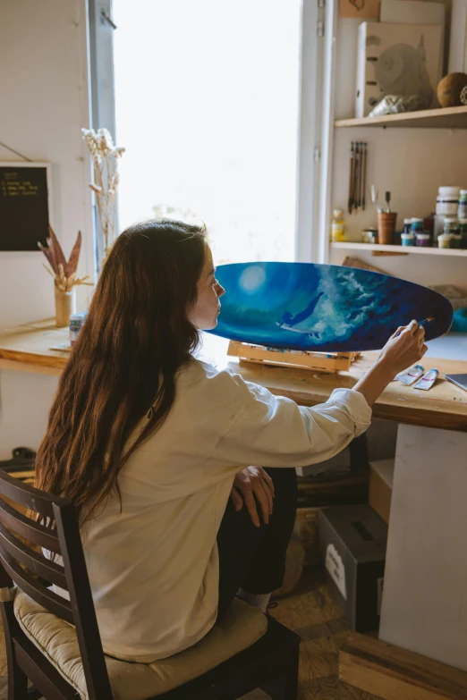 a woman sitting at a desk in front of a computer, an airbrush painting, by Julia Pishtar, pexels contest winner, process art, skateboard art, blue translucent resin, view from the side, oil on wood
