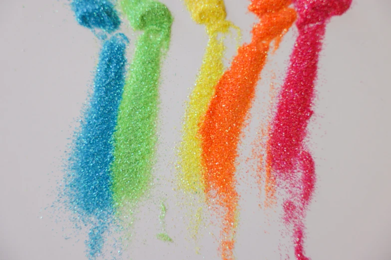 a close up of colored sand on a white surface, a stipple, inspired by George Aleef, pexels, rainbow coloured rockets, fluo details, pixie dust magic, flowing neon-colored silk