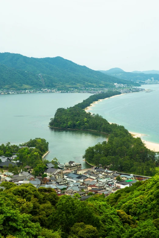 a large body of water sitting on top of a lush green hillside, inspired by Tanomura Chikuden, mingei, beaches, town, white sand beach, grand majestic mountains