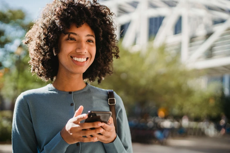 a close up of a person holding a cell phone, dark short curly hair smiling, surrounding the city, realistic »