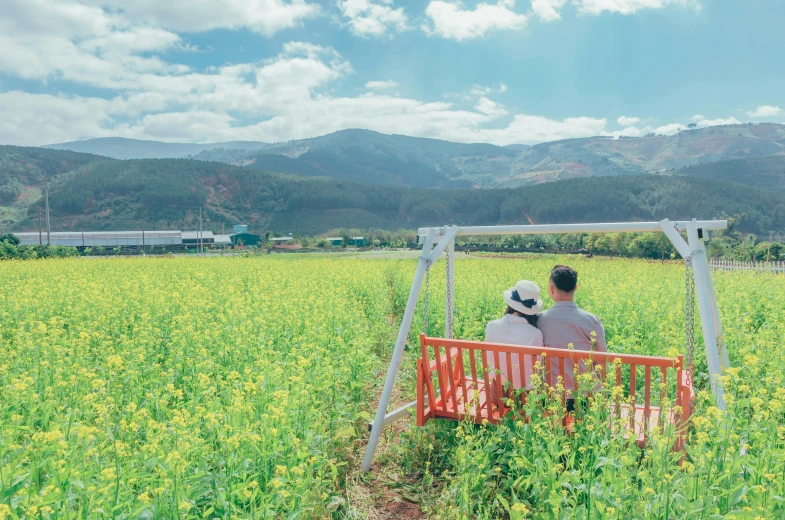 a man and a woman sitting on a bench in a field, a picture, by Tadashige Ono, unsplash, color field, hong soonsang, idyllic and fruitful land, with flower fields as foreground, take off