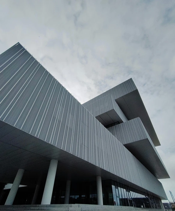 a very tall building with a lot of windows, inspired by David Chipperfield, unsplash, brutalism, museum exposition, large overhangs, grey sky, wide angle exterior 2022