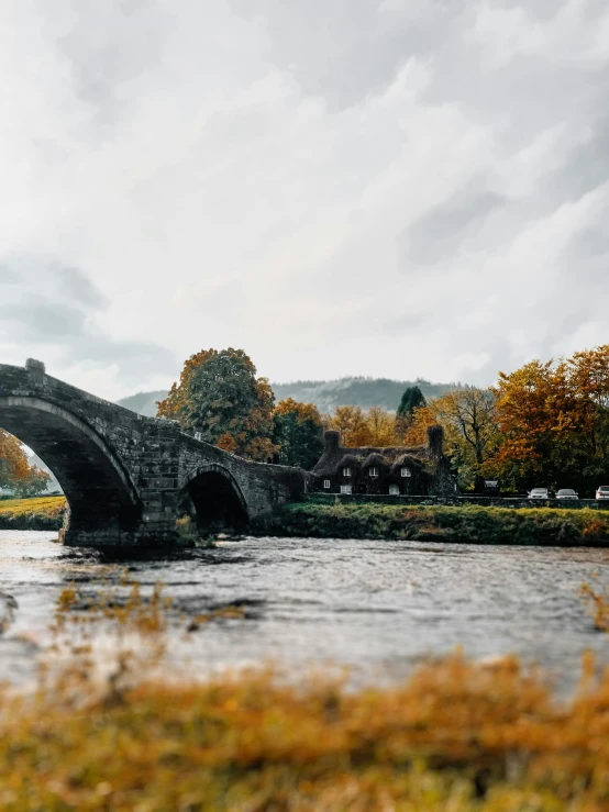 a stone bridge over a body of water, black mountains, during autumn, exterior shot, building along a river