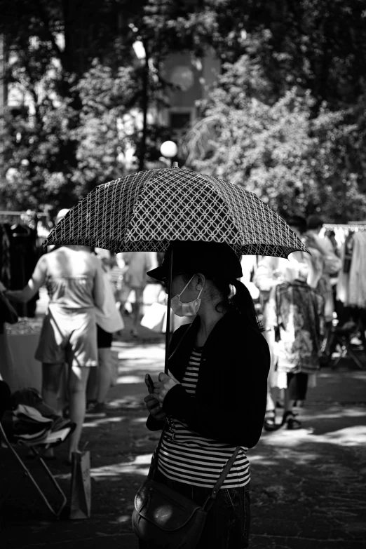 a black and white photo of a woman holding an umbrella, inspired by Vivian Maier, unsplash, hat covering eyes, vendors, hot day, woman