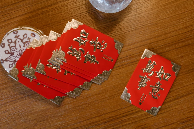 a couple of red envelopes sitting on top of a wooden table, 8 intricate golden tenticles, pair of keycards on table, drink, zoomed in