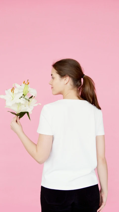 a woman holding a bouquet of flowers on a pink background, inspired by Marina Abramović, shutterstock contest winner, minimalism, dressed in a white t-shirt, lily, 15081959 21121991 01012000 4k, back