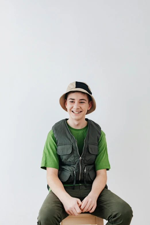 a man sitting on top of a cardboard box, wearing green clothing, portrait of a japanese teen, technical vest, he is wearing a hat