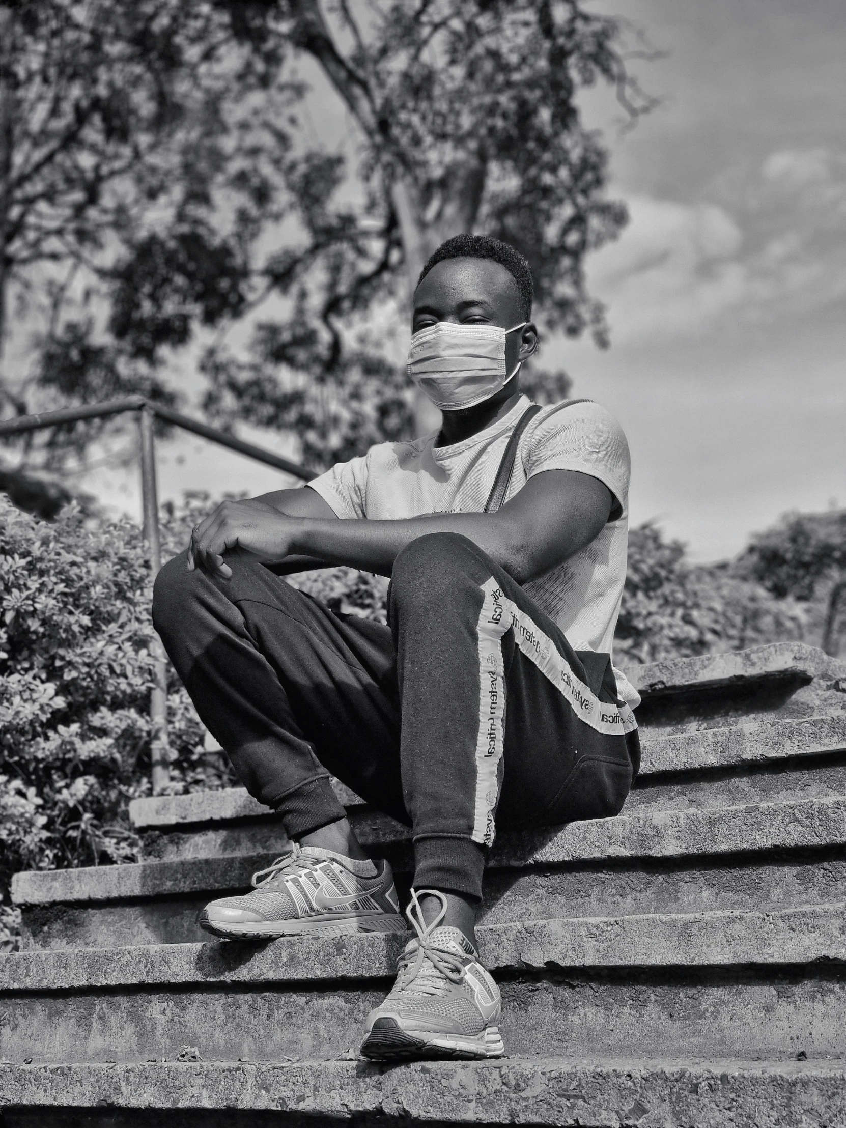 a black and white photo of a man wearing a face mask, a black and white photo, by Maxwell Bates, black teenage boy, sitting down casually, mongezi ncaphayi, instagram post