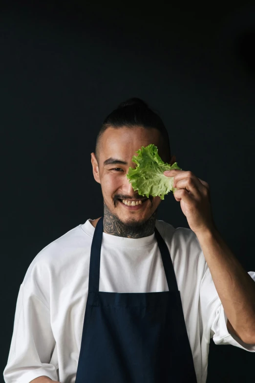 a man holding a lettuce in front of his face, a picture, inspired by Kanō Naizen, pexels contest winner, white apron, profile image, short goatee, subject is smiling