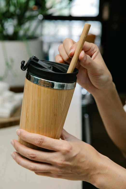 a close up of a person holding a cup of coffee, made of bamboo, top lid, demolition, spoon placed