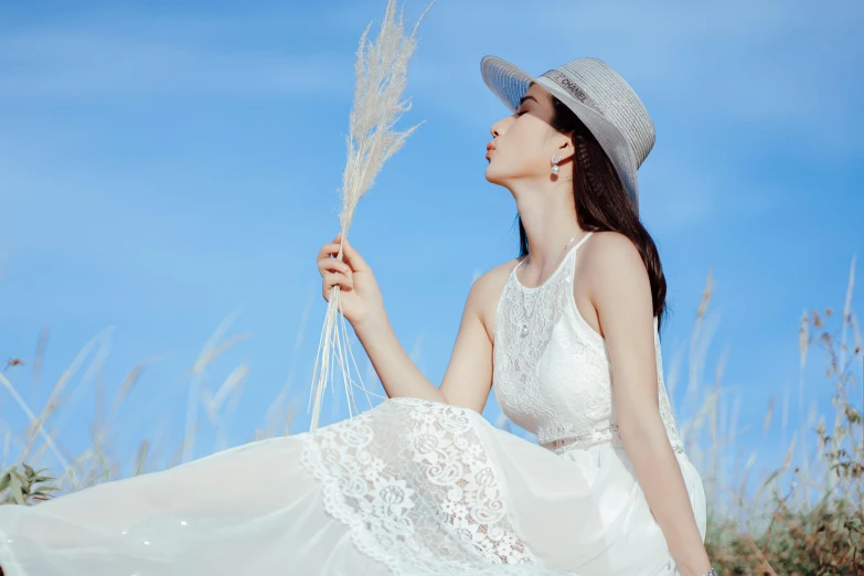 a woman in a white dress and hat sitting in a field, pexels contest winner, korean women's fashion model, silver，ivory, white and blue, straw