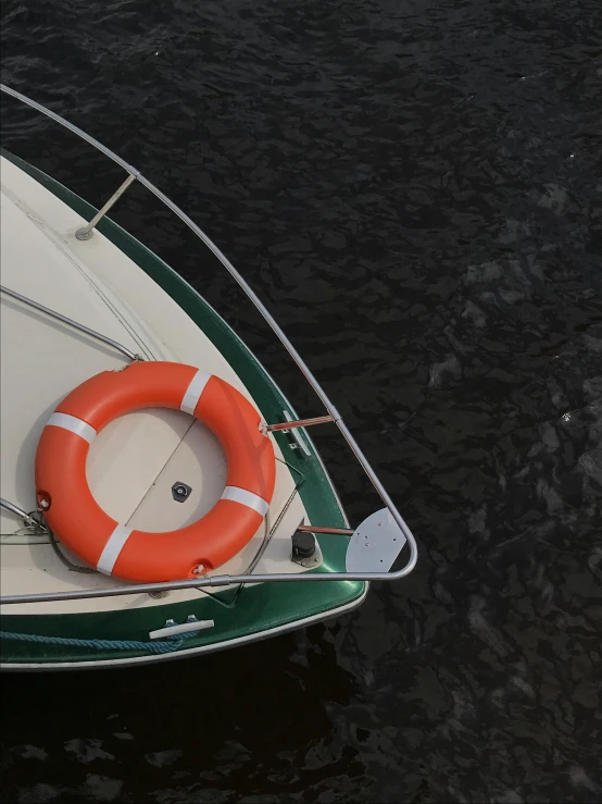 a green and white boat sitting on top of a body of water, dark grey and orange colours, camera looking down upon, circular, emergency
