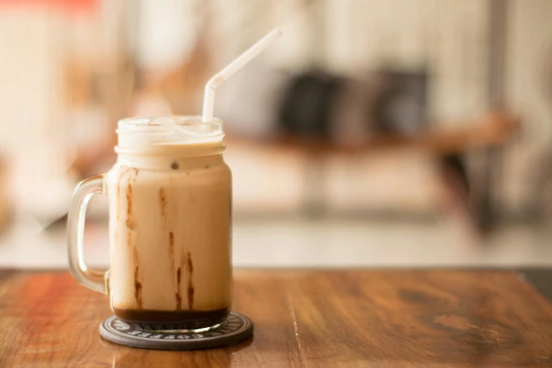 a glass of iced coffee sitting on top of a wooden table, trending on unsplash, square, milkshake, australian, jen atkin