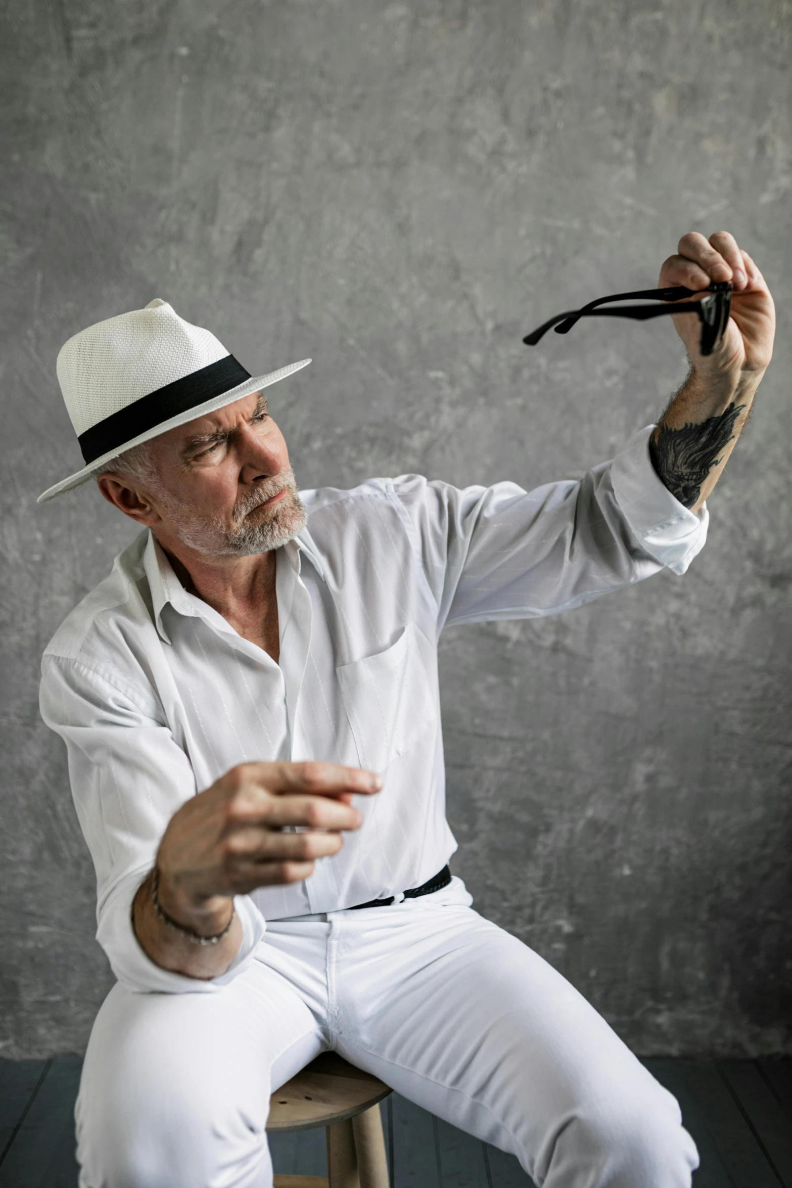 a man sitting on a stool holding a pair of scissors, inspired by Joseph Beuys, unsplash, white hat, grey beard, patrick stewart, hunter s thompson