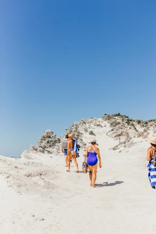 a group of people walking on top of a sandy beach, blue and white, ladies, lush surroundings, prop rocks