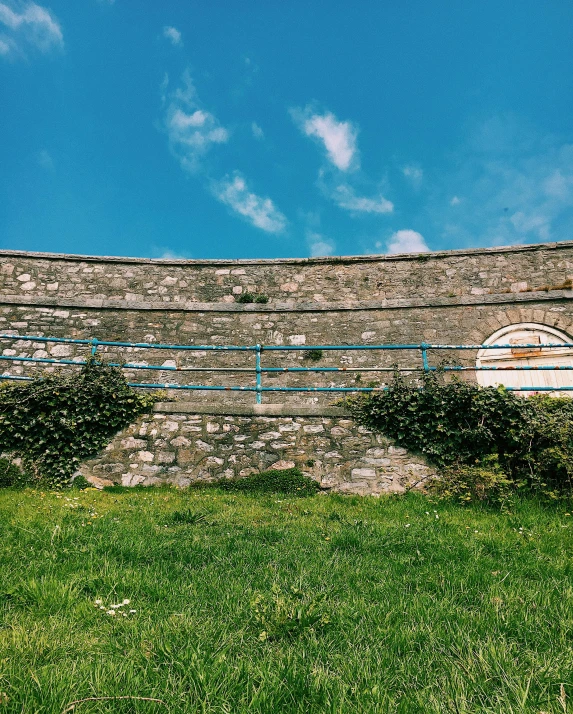 a red fire hydrant sitting on top of a lush green field, an album cover, by Rachel Reckitt, unsplash, graffiti, castle wall, sky blue, panoramic, white stone arches