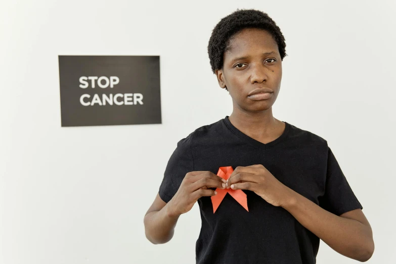 a woman holding a red ribbon in front of a stop cancer sign, by Lily Delissa Joseph, pexels contest winner, renaissance, kara walker, 2 4 years old, museum photograph, marie curie