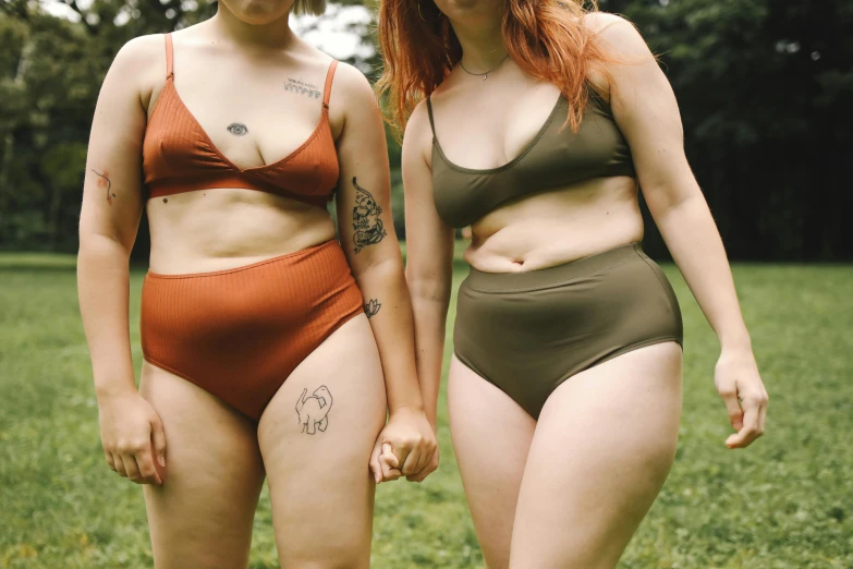 a couple of women standing on top of a lush green field, inspired by Elsa Bleda, trending on pexels, renaissance, wearing two - piece swimsuit, overweight, deep earthy colours, bottom body close up