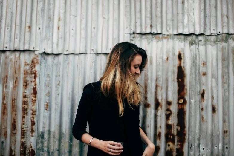 a woman standing in front of a metal wall, by Alice Mason, minimalism, rugged black clothes, portrait featured on unsplash, vsco film grain, thin lustrous hair