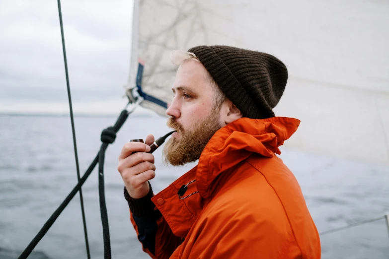 a man on a boat smoking a pipe, inspired by mads berg, pexels contest winner, orange jacket, thick braided beard, 26 year old man on a sailboat, male polar explorer