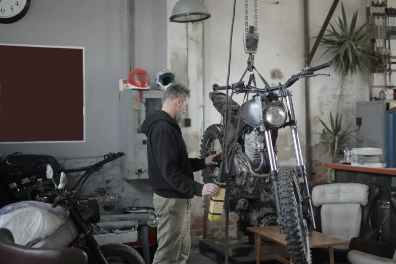 a man standing next to a motorcycle in a garage, blacksmith product design, filmstill, hanging, mechanised